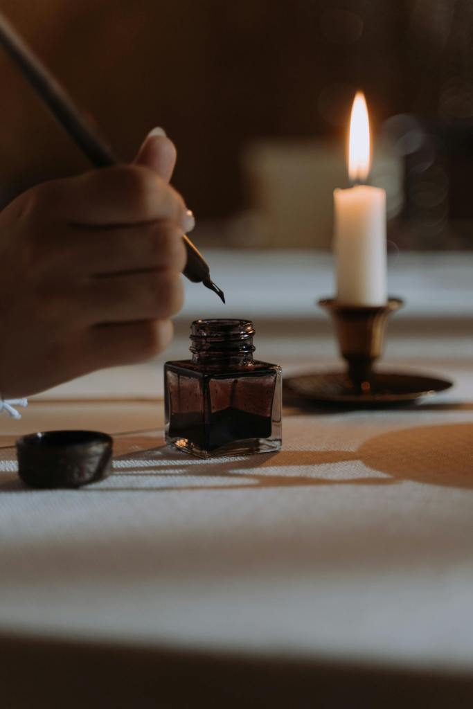 Picture of hand with a quill writing and a candle in the background. 